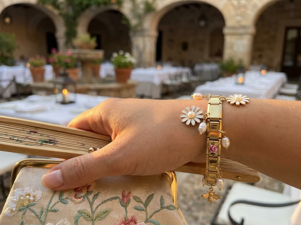 A wedding guest holding a clutch and a fan, wearing a gold charm bracelet